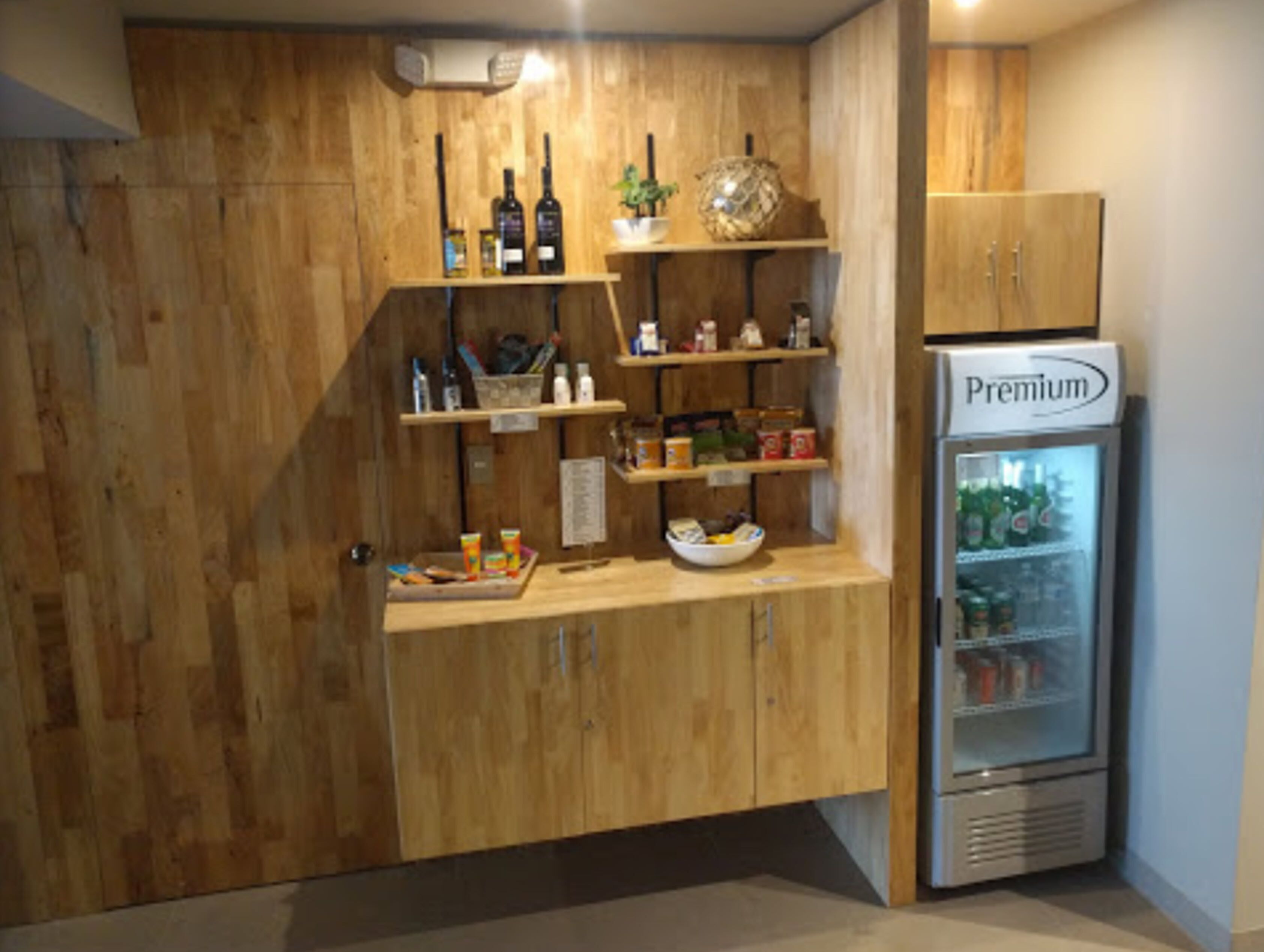A kitchenette with wooden cabinets, shelves with bottles, a bowl of fruit, and a refrigerator labeled "Premium".