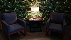 Dos sillones enfrentados con una mesita entre ellos, una lámpara sobre la mesa y un fondo de follaje verde.