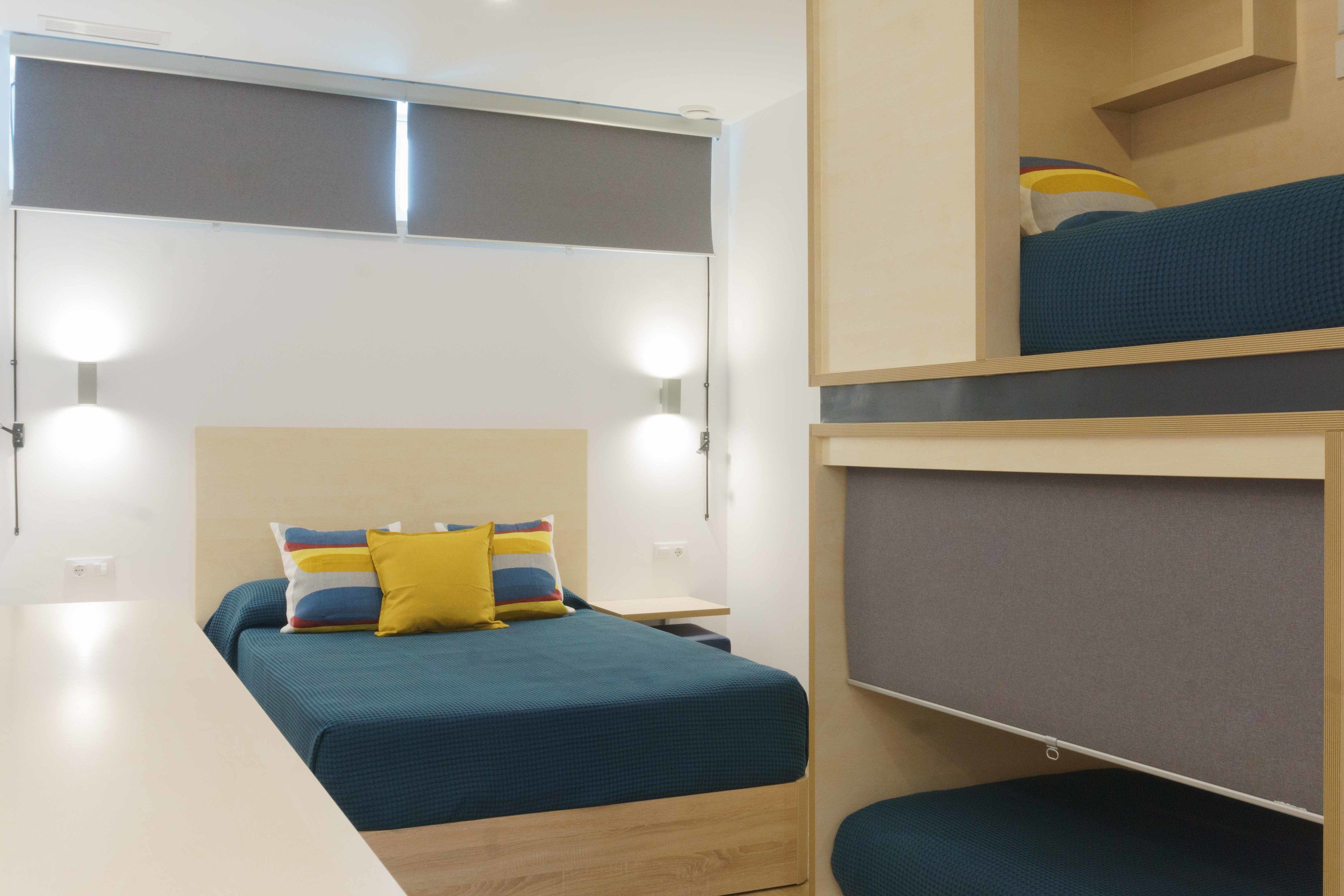 A compact hotel room with a bunk bed, a bedside table, and a desk.
