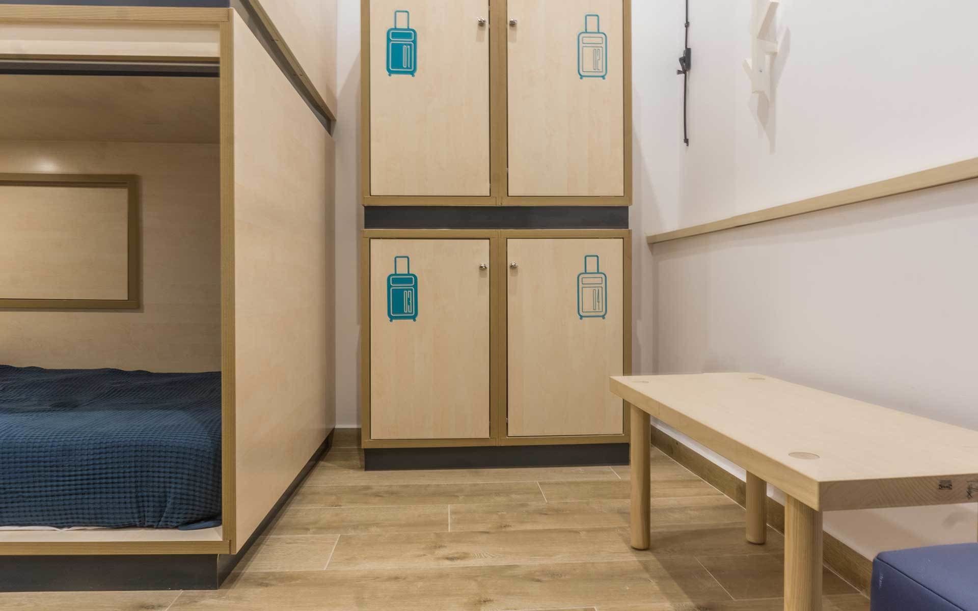 A compact room with a bed, a desk, and two cabinets with luggage icons, indicating a self-service storage area.