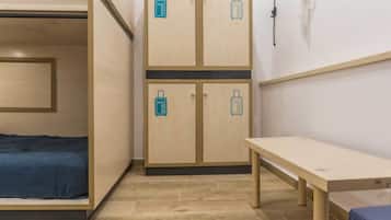 A compact room with a bed, a desk, and two cabinets with luggage icons, indicating a self-service storage area.