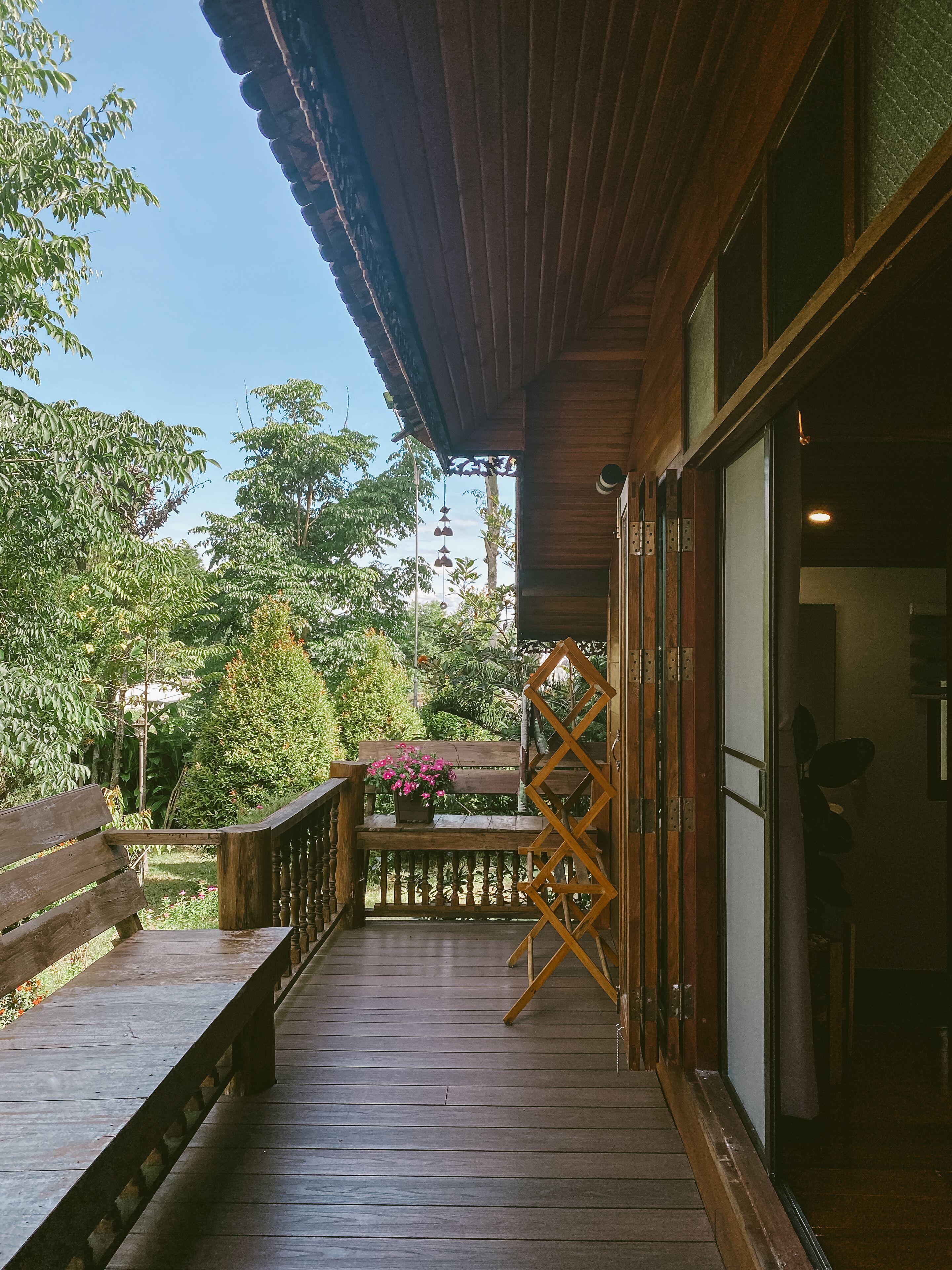 A wooden deck with a bench and a potted plant, leading to a building with a glass door.