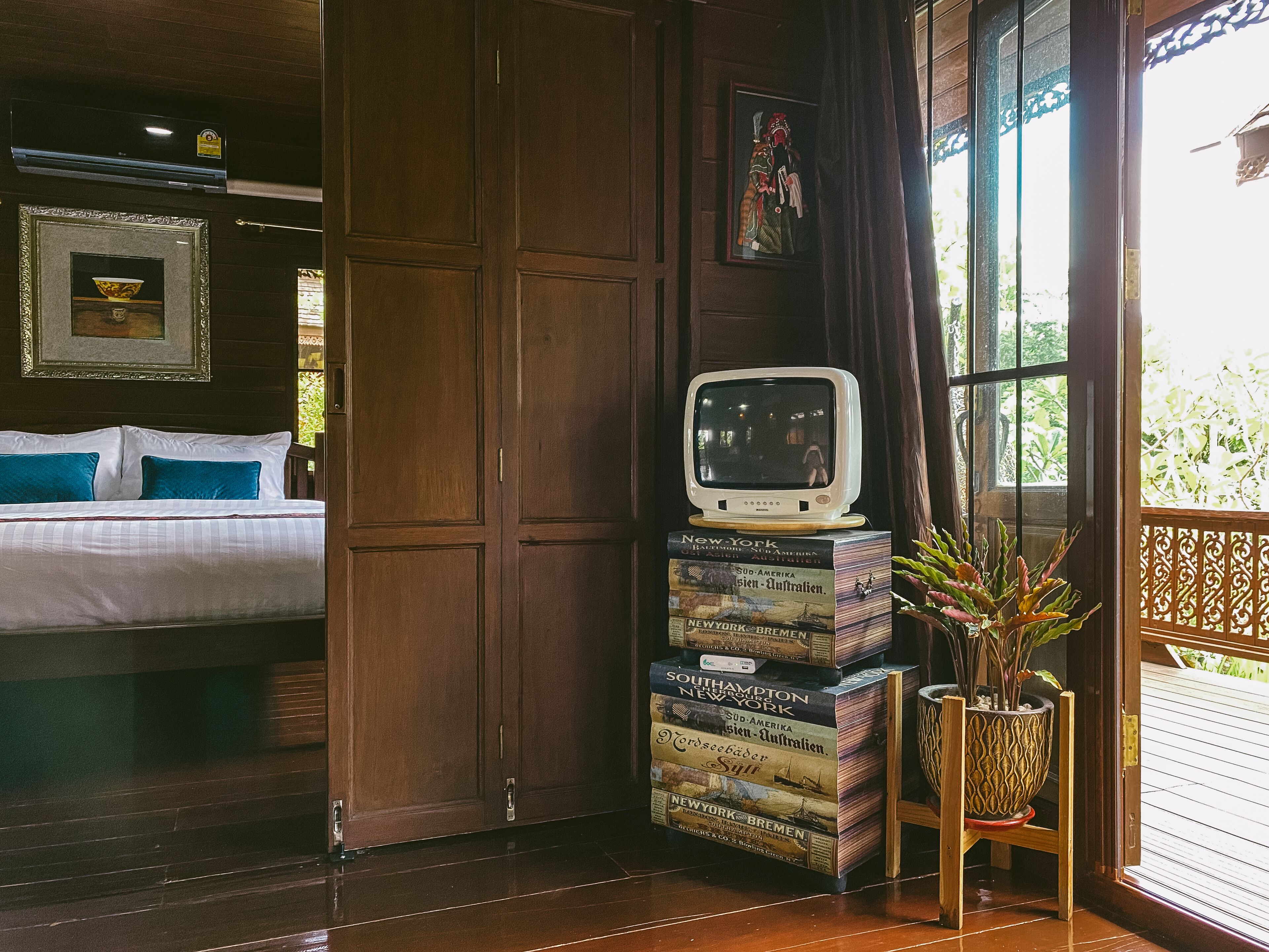 A hotel room with a bed, a television on a stack of books, and a potted plant.