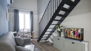 A modern living room with a staircase, a dining area, and a television on a cabinet.