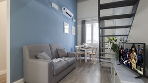 A modern living room with a grey sofa, a dining table with chairs, and a staircase with a railing.