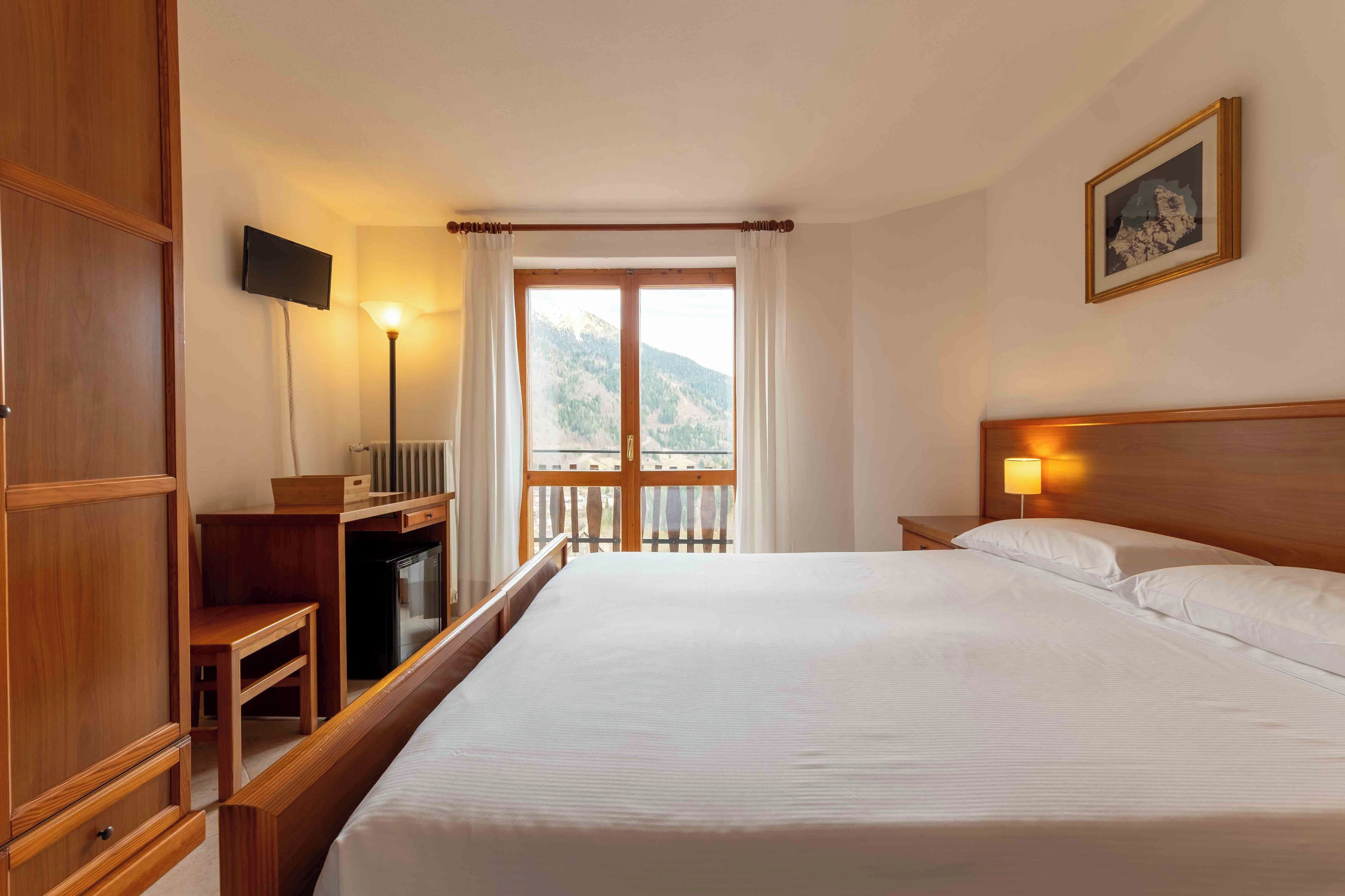 Ein Hotelzimmer mit Bett, Schreibtisch, Fernseher, Nachttisch, Lampe und einem Fenster mit Bergblick.