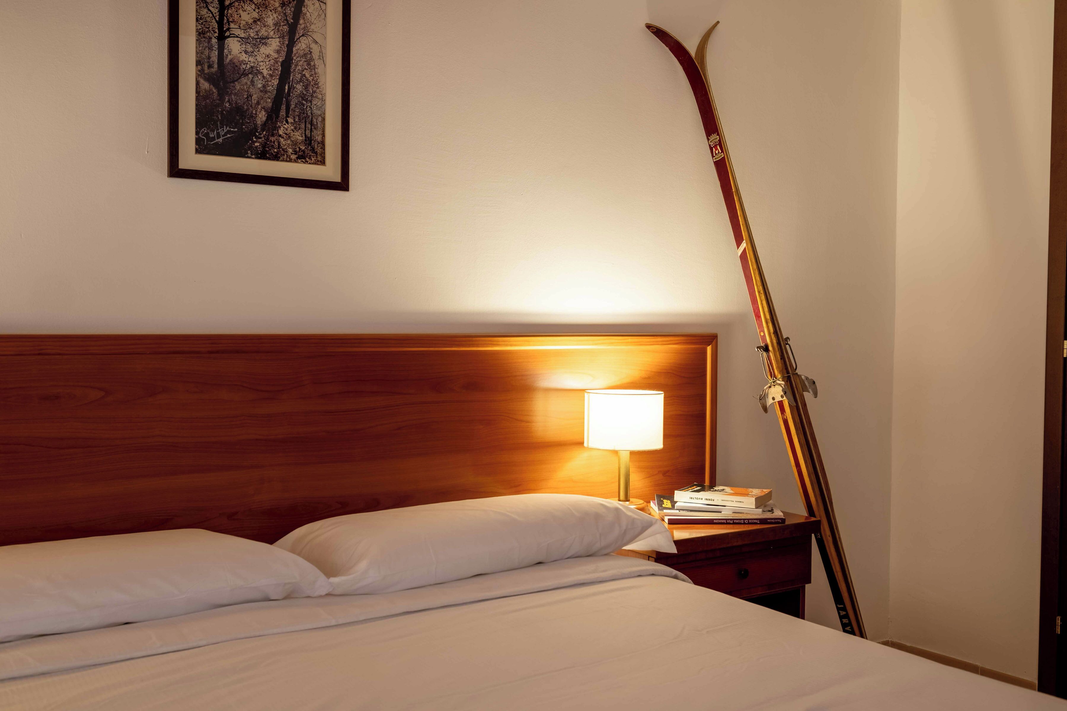 Een hotelkamer met een houten hoofdeinde, een bedlamp, een ski stok en een ingelijst schilderij aan de muur.