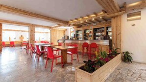 A restaurant with wooden beams, red chairs, a bar area, and a stone floor. -  Miravalle Supersport Hotel (Forni Avoltri)