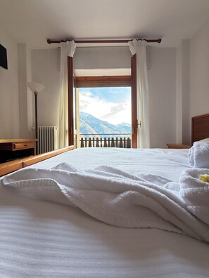 Une chambre d’hôtel avec un lit, une vue sur les montagnes, une tête de lit en bois et un radiateur.