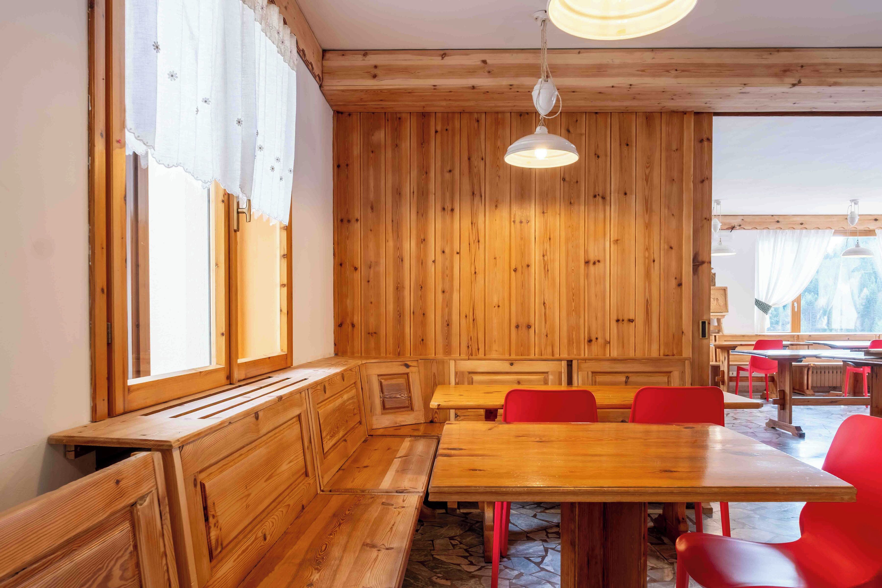 Un intérieur en bois avec des bancs et des tables, de grandes fenêtres et un luminaire suspendu.