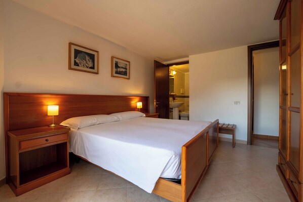 Une chambre d’hôtel avec un lit en bois, des tables de chevet, une petite table de nuit, un petit banc et une armoire.