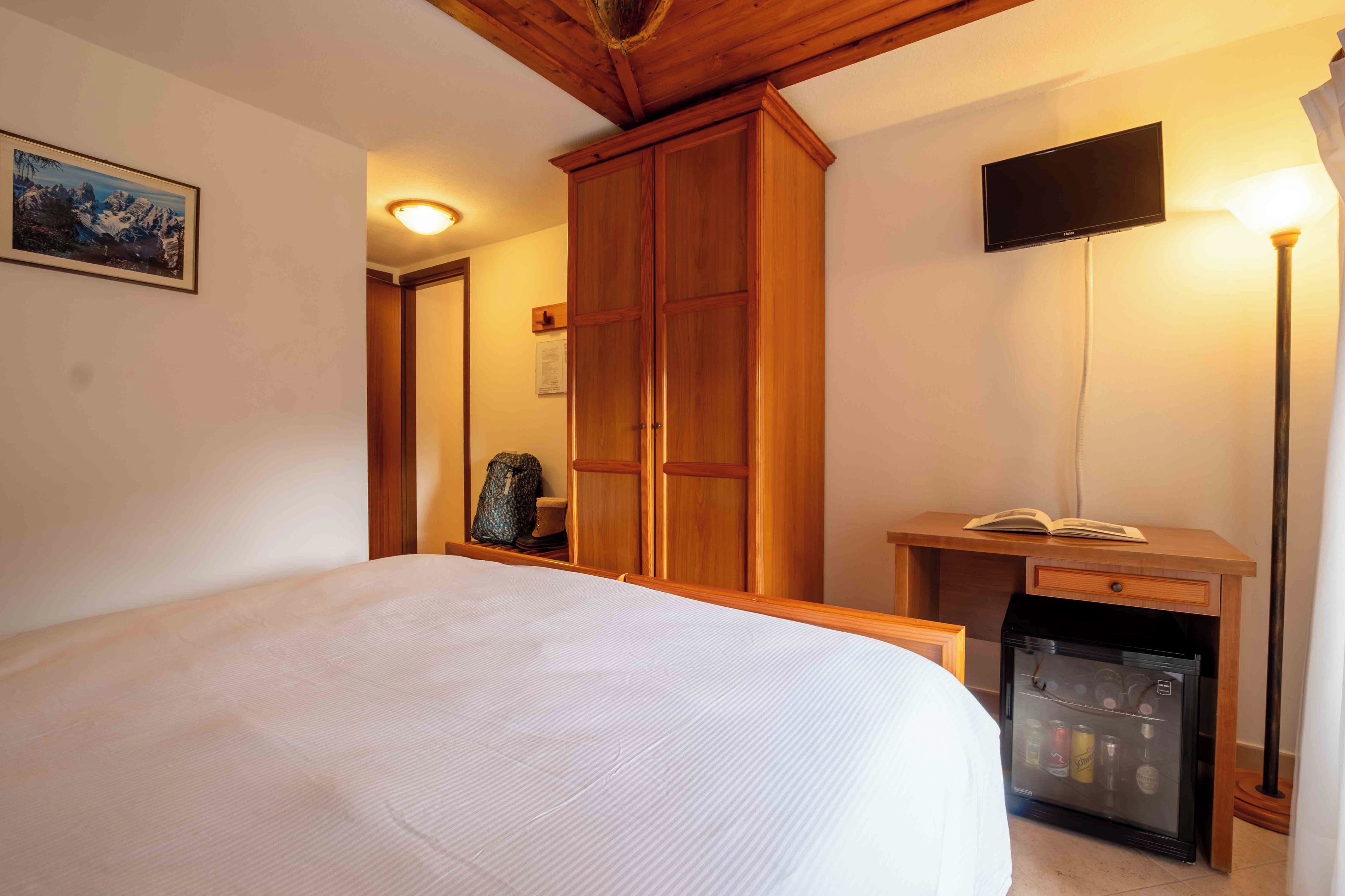 A bedroom with a bed, a wardrobe, a television, and a minibar.