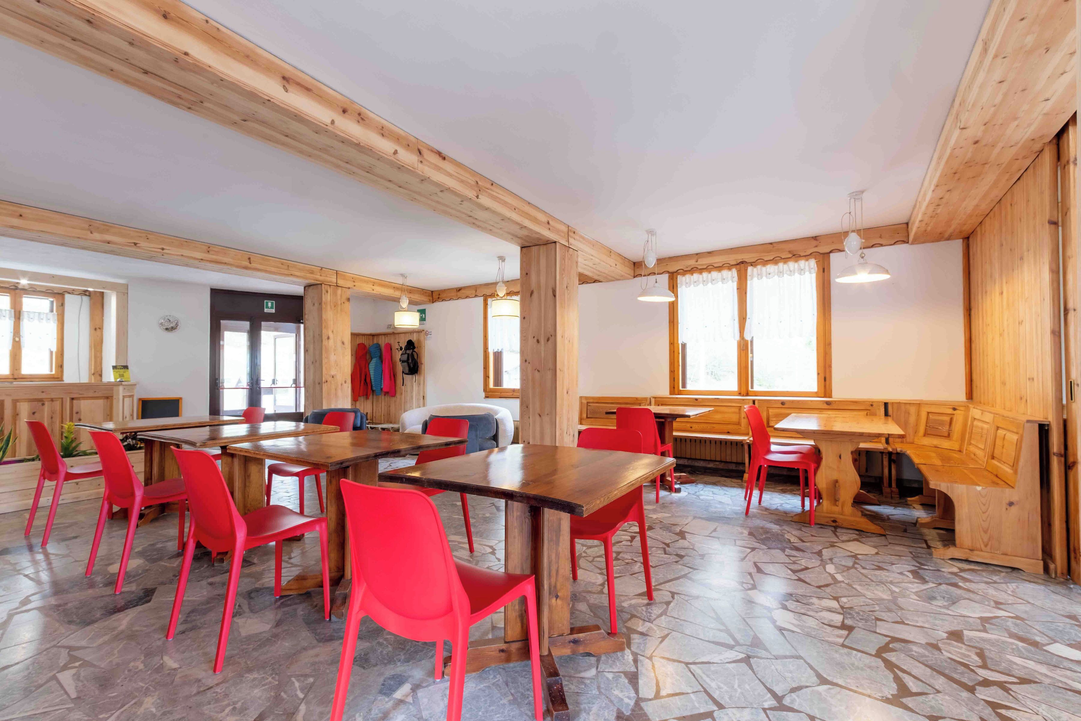A spacious room with wooden beams, a stone floor, and red chairs around a central table.