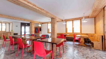 A spacious room with wooden beams, a stone floor, and red chairs around a central table.
