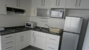 A compact kitchen with white cabinets, a microwave, a toaster, and a refrigerator.