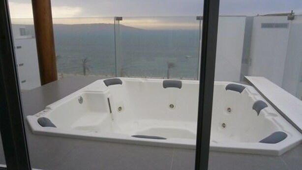 A hot tub with a panoramic ocean view, positioned on a balcony with glass railings.