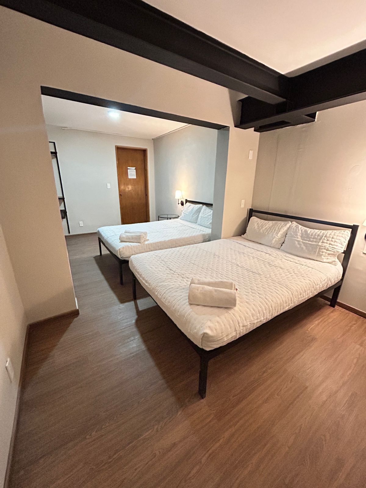 Een hotelkamer met twee bedden, houten vloeren en een deur die naar een andere kamer leidt.