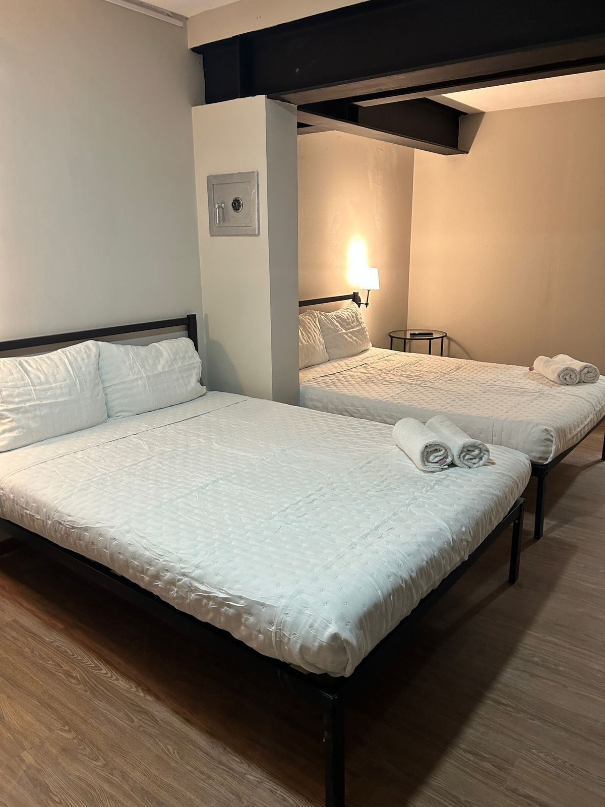 Two beds with white bedding, a wall-mounted light, and a small table.