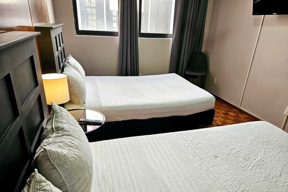 A hotel room with two beds, a nightstand, a lamp, and a TV.