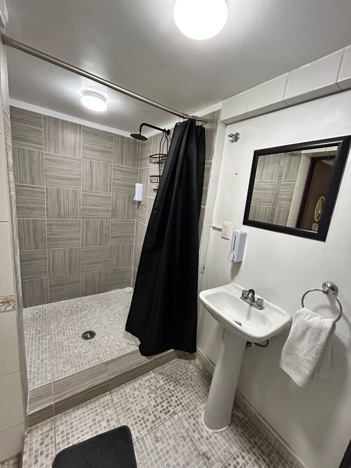 Un baño con ducha, lavamanos y espejo.