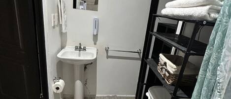 A small, compact bathroom with a toilet, sink, and a shelf with towels.