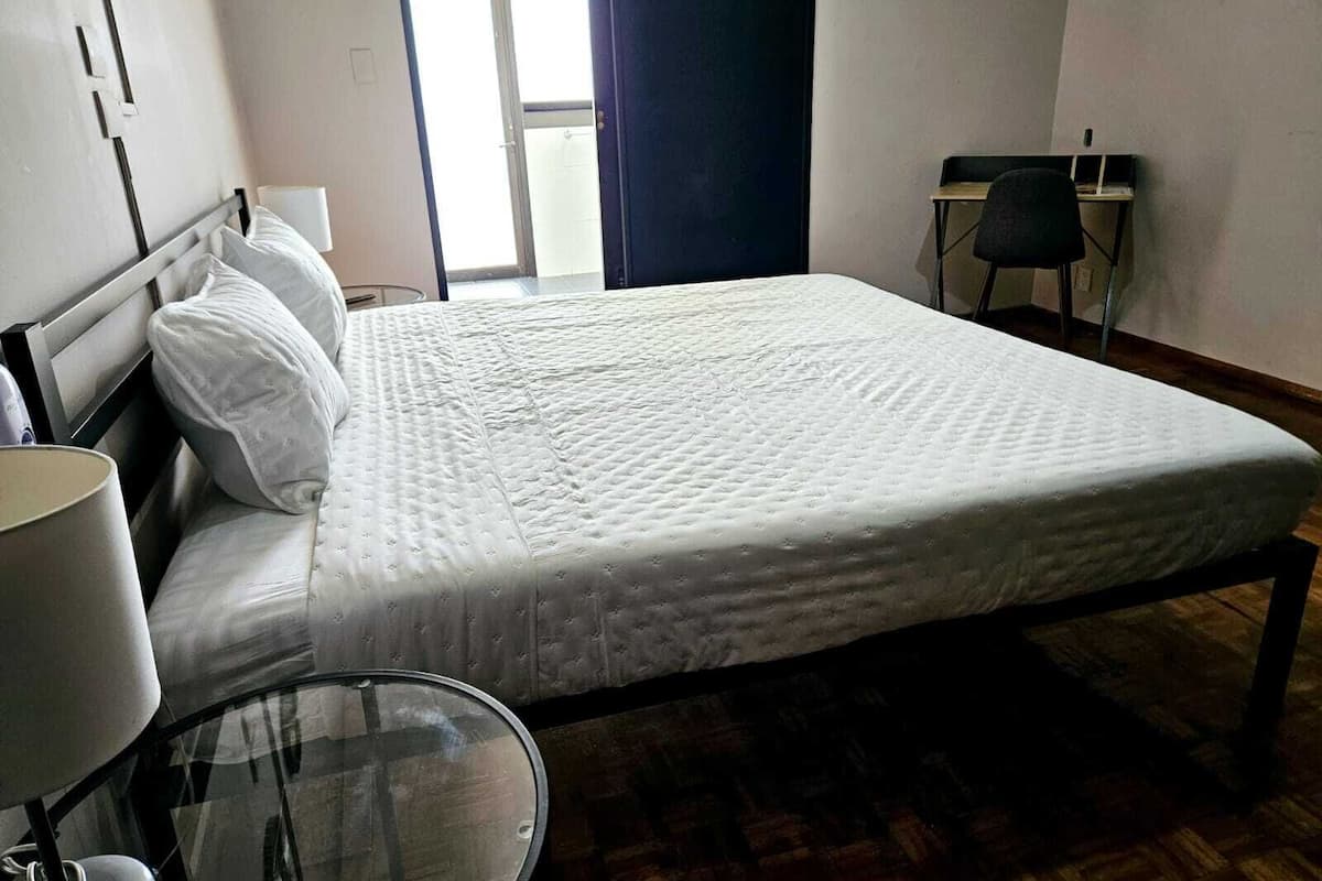 A neatly arranged hotel room with a bed, a glass table, a chair, and a desk.