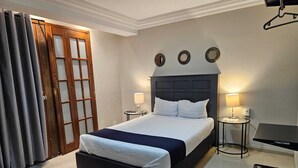 A hotel room with a large bed, two bedside tables with lamps, a wooden door, and a small desk with a chair. - Hotel Singular Coyoacán (Mexico City)