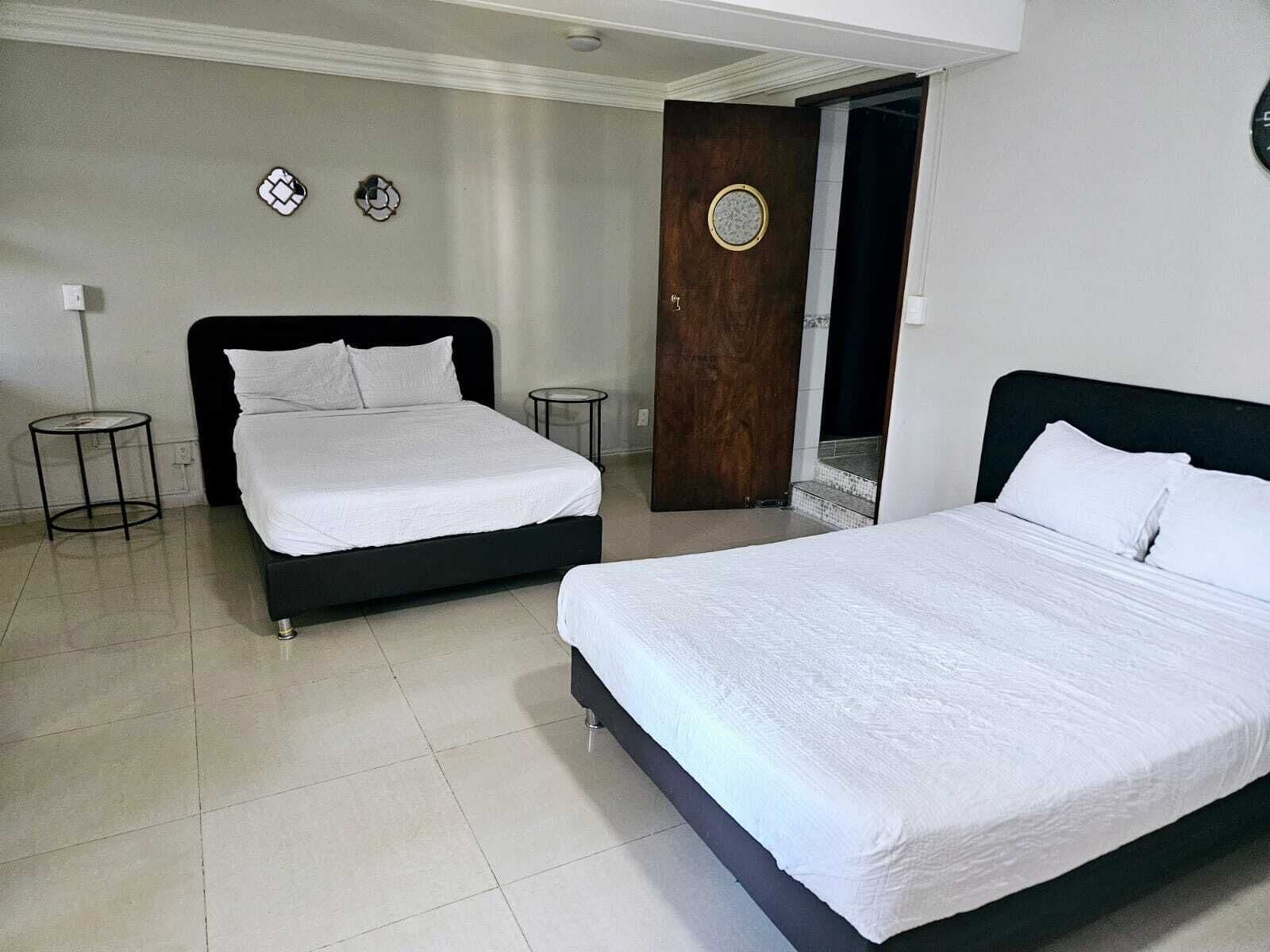 Habitación de hotel con dos camas, un espejo redondo y una puerta con un ventanal circular.