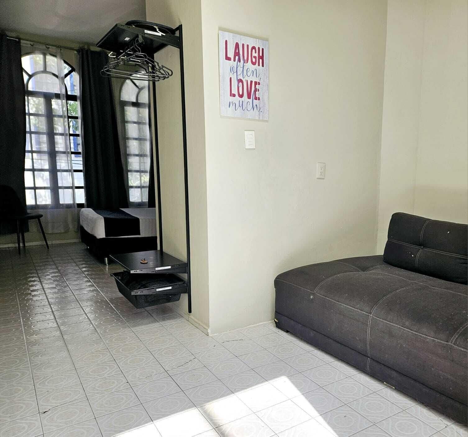 A living room with a dark sofa, a small table, and a sign that reads "LAUGH (often) LOVE".