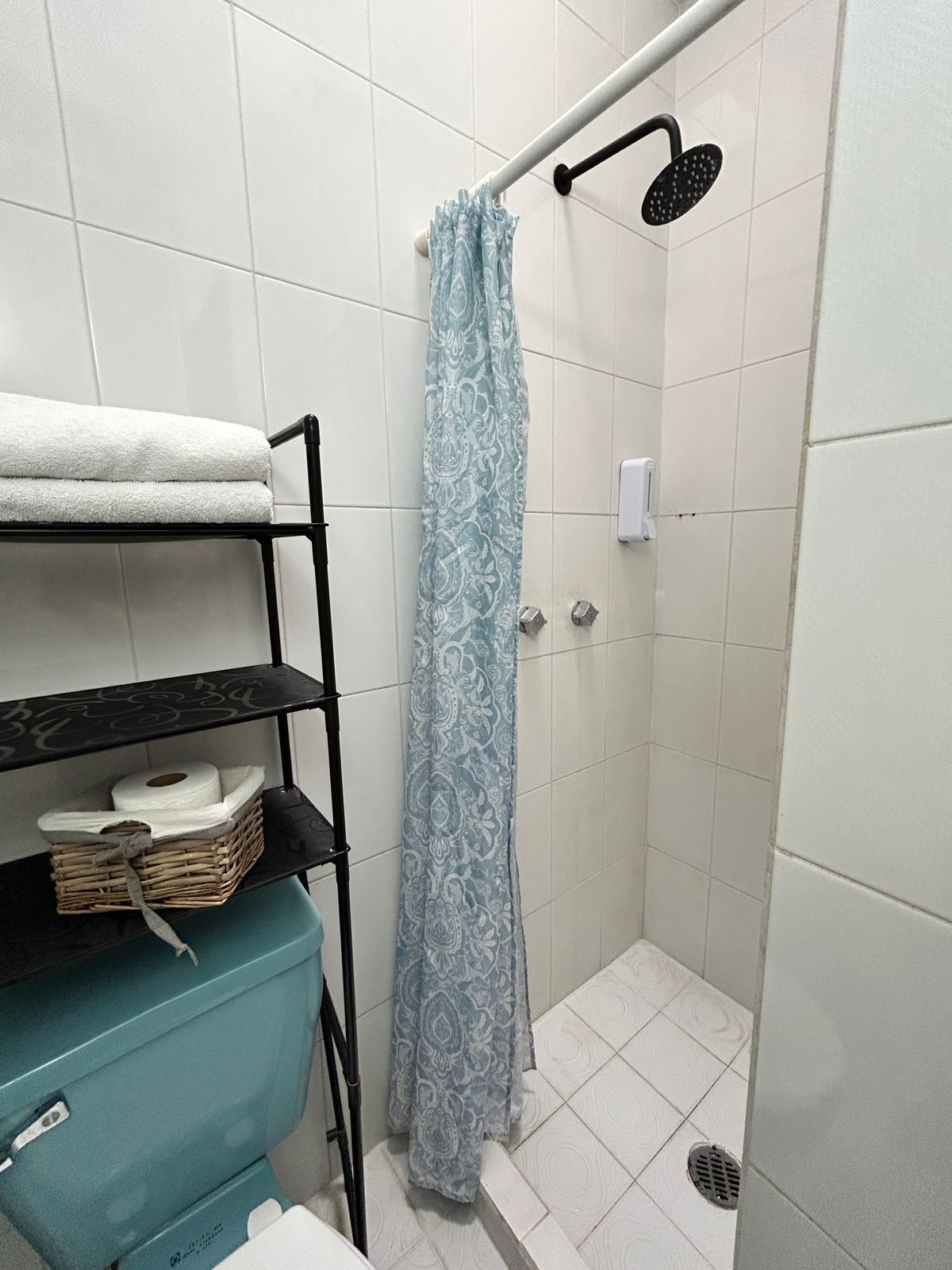 A small, tiled bathroom with a shower, a towel rack, and a shelf with toiletries.
