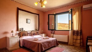 Um quarto com cama, mesas de cabeceira, cortinas numa janela e vista para o exterior.