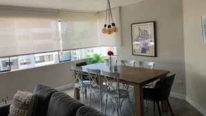 A dining area with a wooden table, white chairs, a hanging light fixture, and a framed picture on the wall. - MLA apartments - 28 de Julio (Lima)