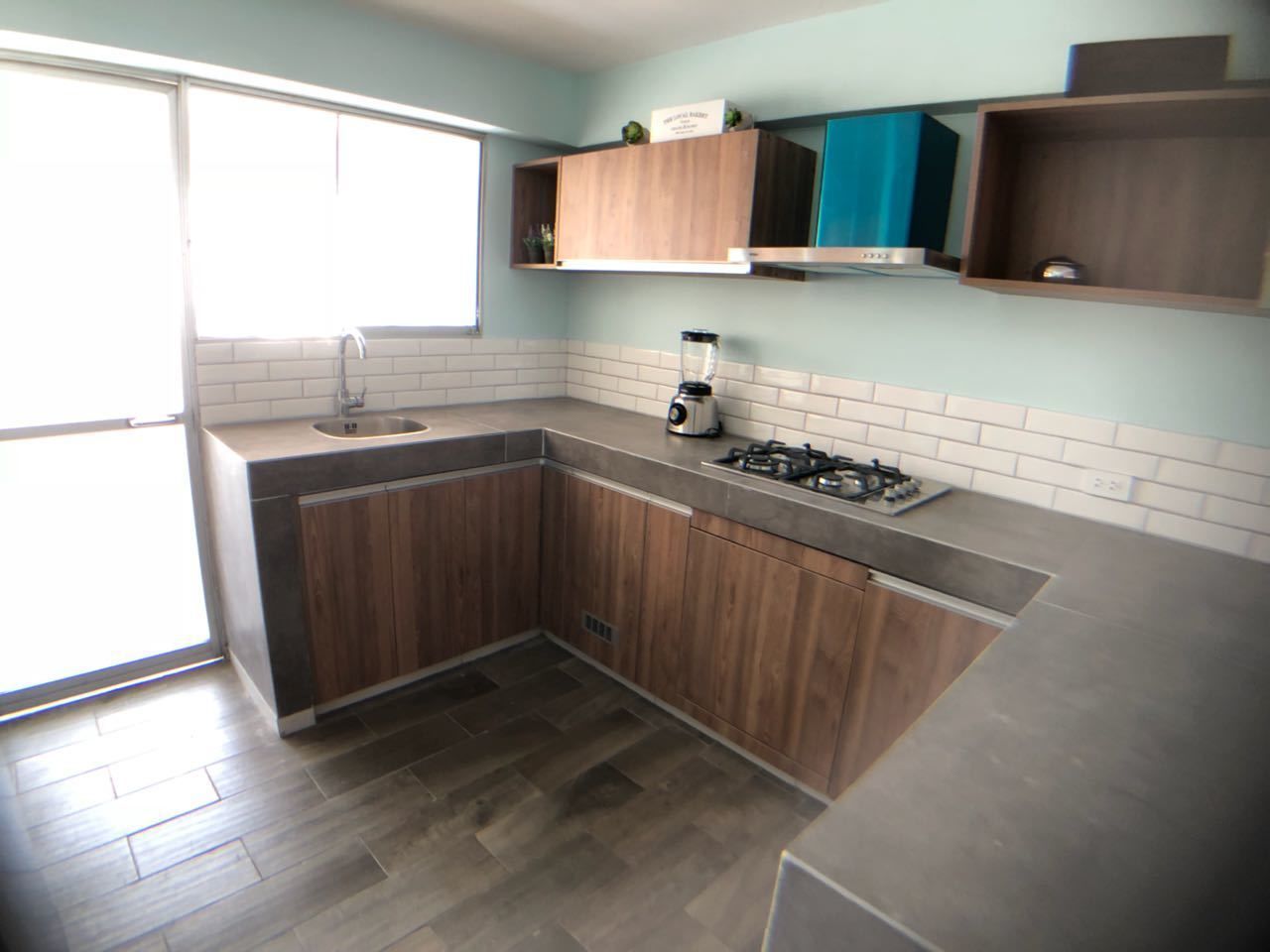 Une cuisine avec des meubles de rangement en bois, une cuisinière à gaz et un mixeur posé sur le plan de travail.