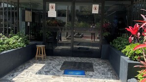 A modern building entrance with glass doors, a small outdoor seating area, and a tiled patio. - MLA apartments - 28 de Julio (Lima)
