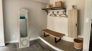 A hallway with a mirror, bench, wooden cabinet, and wall-mounted shelves with baskets and a plant. - MLA apartments - 28 de Julio (Lima)