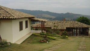 Una casa tradicional amb teulada, un petit jardí amb un camí de pedra i vista a les colines de fons.