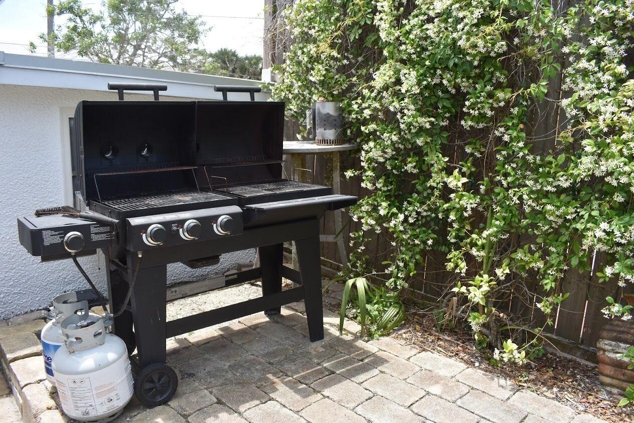 A portable barbecue grill with a gas tank, set on a patio with a brick floor.