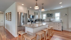 Una cocina moderna con armarios blancos, una isla grande con taburetes, electrodomésticos de acero inoxidable e iluminación colgante.