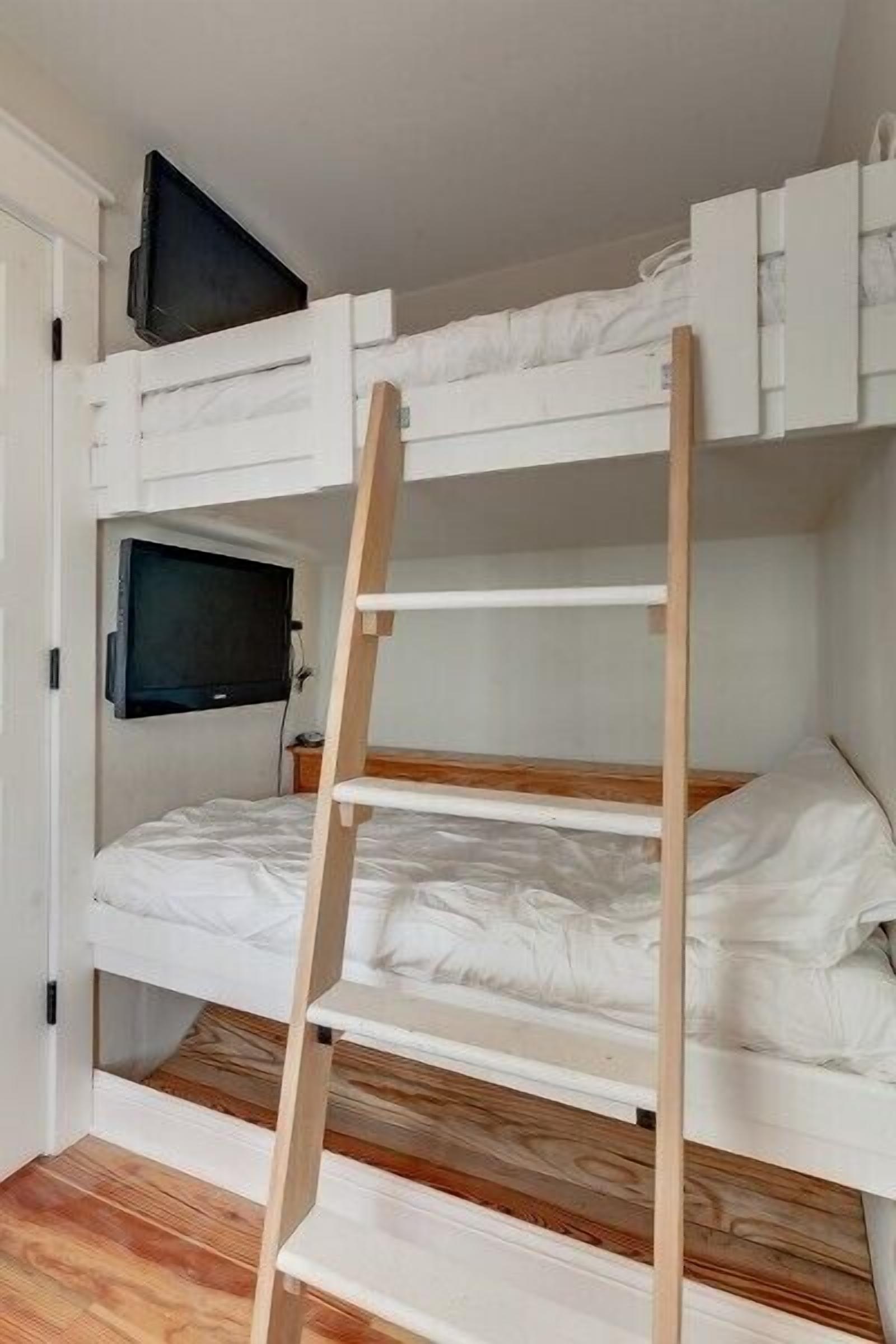 Un lit superposé avec un téléviseur fixé au-dessus, un plancher en bois et une porte blanche.