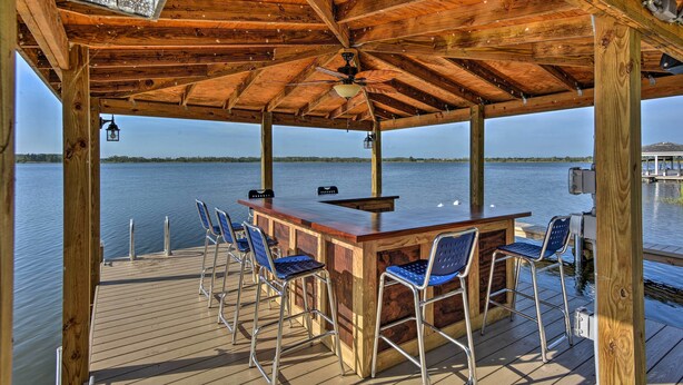 Eine Holzterrasse mit Bar, Stühlen und Blick auf das Wasser.