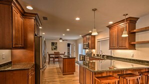 Eine moderne Küche mit Holzschränken, einem Edelstahlkühlschrank, einer Granitarbeitsplatte und einer zentralen Kochinsel mit Barhocker.