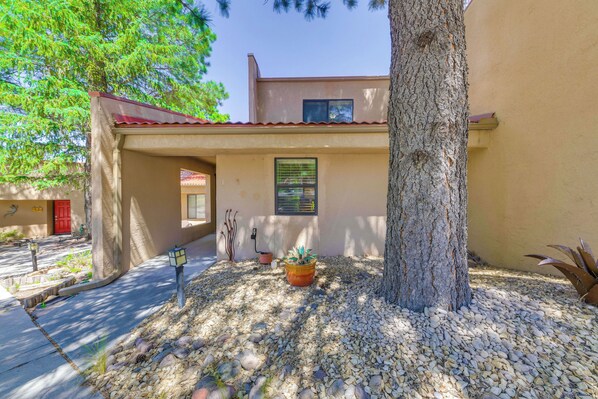 A building with a red roof, a large tree, and a potted plant in the foreground. - Patio & Mountain View! Ruidoso Golf Condo (Ruidoso)