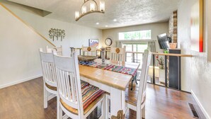 A dining area with a wooden table and white chairs, a chandelier, and a view of the outdoors. - Patio & Mountain View! Ruidoso Golf Condo (Ruidoso)