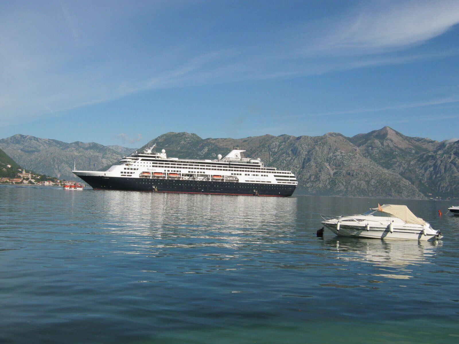 Un gran crucero amarrado en un puerto deportivo, con montañas al fondo.