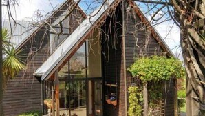 Een modern huis met een schuin dak, grote ramen en een klein terras met buitenmeubels.