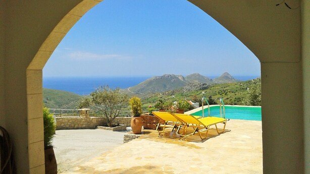 Une terrasse avec une piscine, des chaises longues jaunes et une vue sur l’océan et les montagnes.
