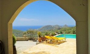 A patio with a pool, yellow lounge chairs, and a view of the ocean and mountains. - Villa Liberty with fantastic view,close to a farm in a traditional village. (Rethymno)