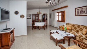 Un salon avec un canapé, une table basse en bois et un téléviseur posé sur un meuble. On y trouve également une table à manger avec des chaises et un lustre.