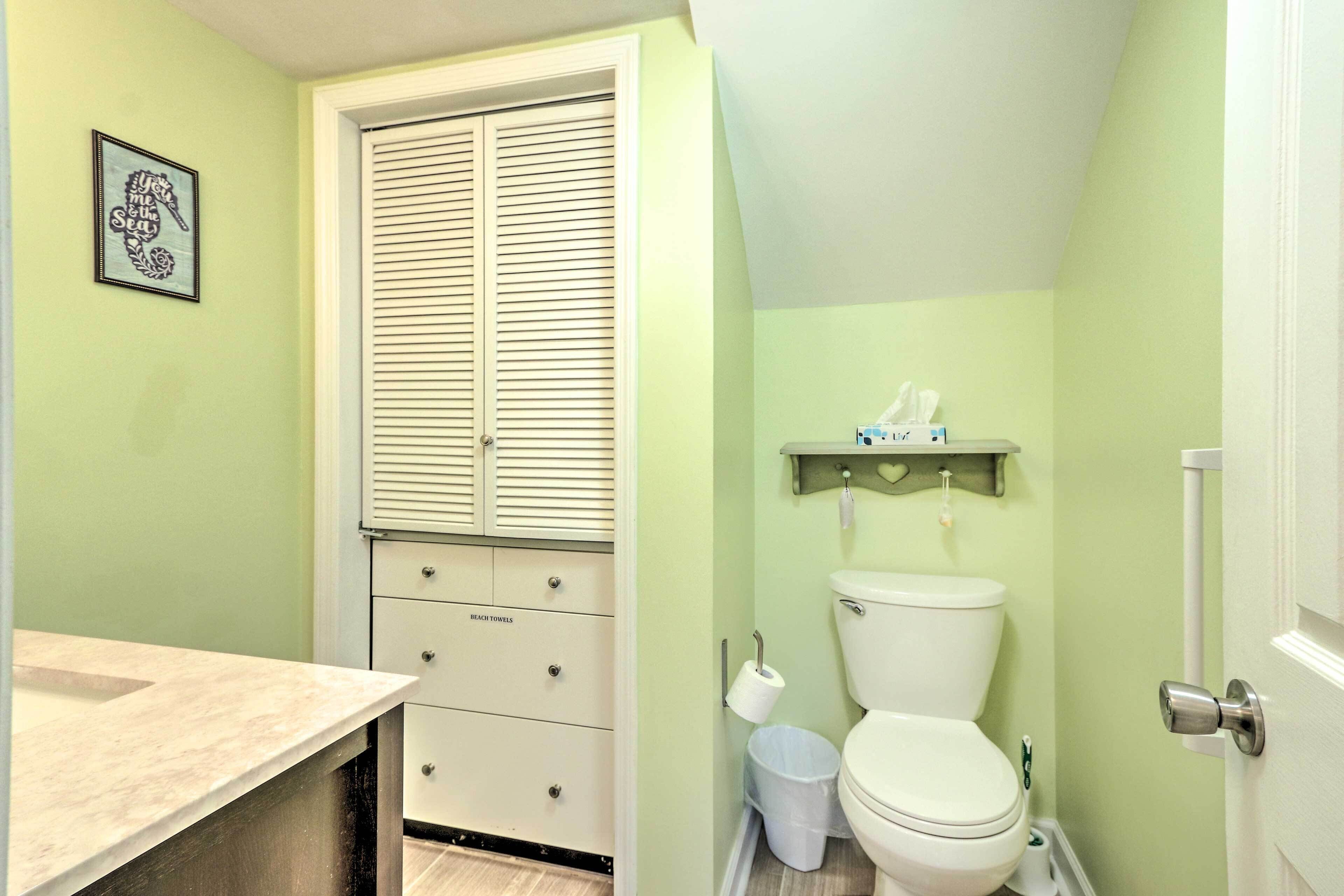 A bathroom with a toilet, a trash can, a towel dispenser, and a cabinet with drawers.