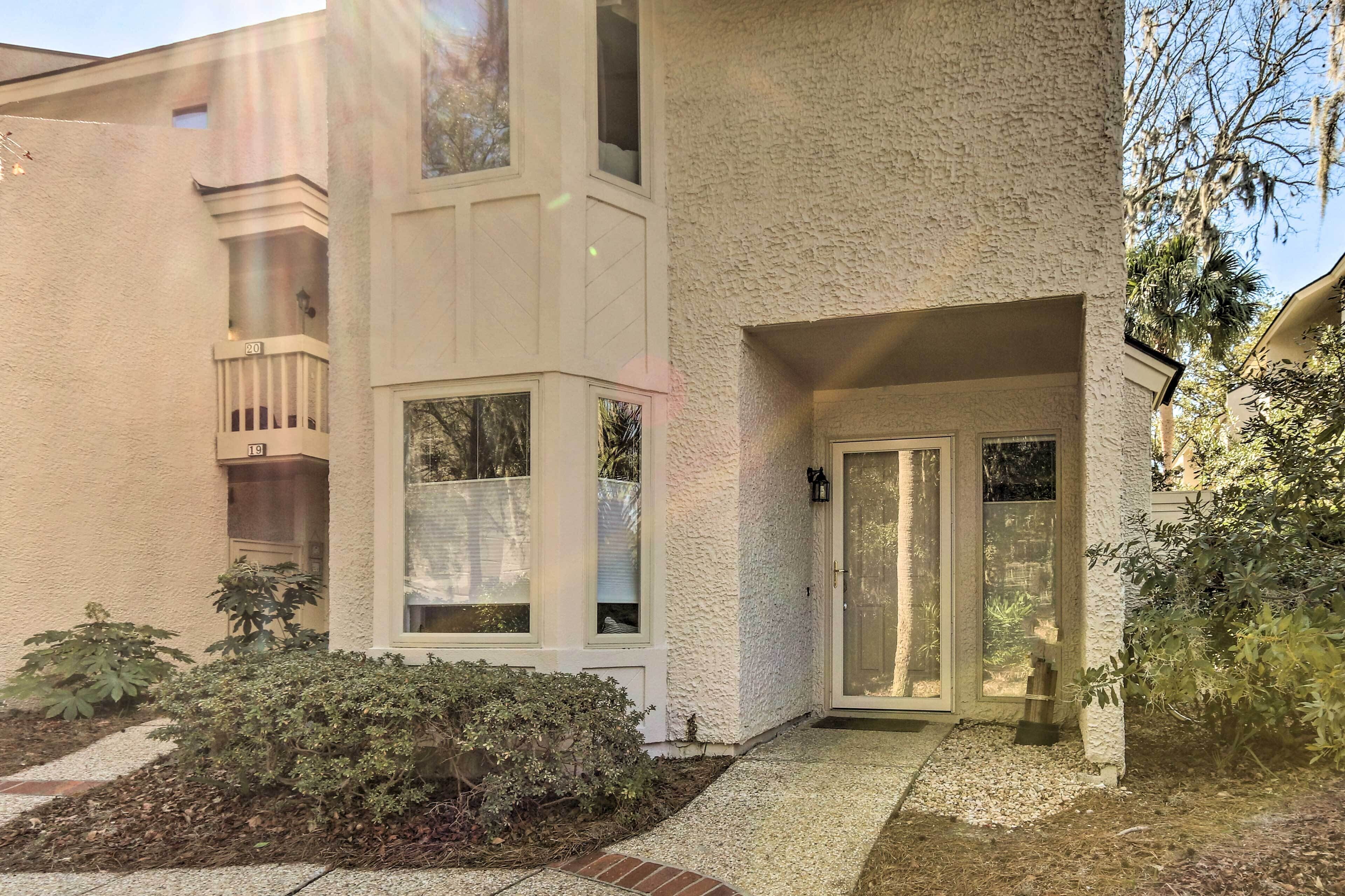 A two-story building with a white exterior, a balcony on the second floor, and a front door with a glass panel.
